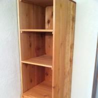 An empty, light-brown wooden bookshelf with three shelves against a plain white wall.