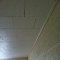 Textured white ceiling tiles meeting a concrete block wall at an angle.