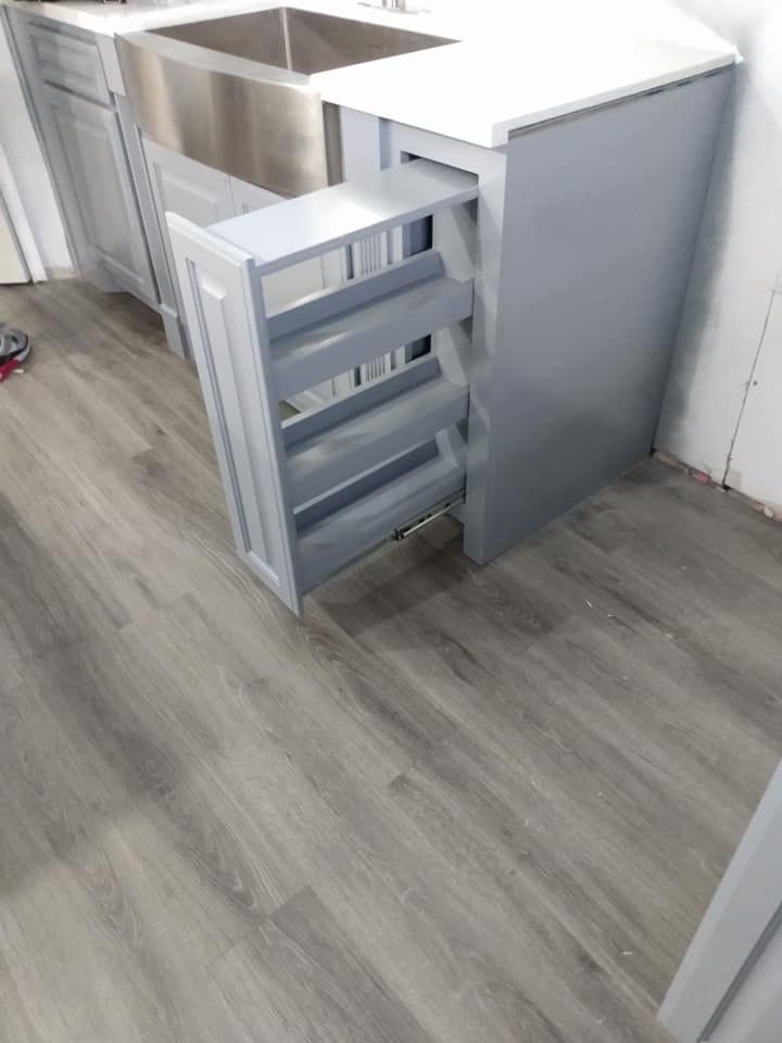 Gray kitchen cabinet with pull-out shelves next to a stainless steel sink.