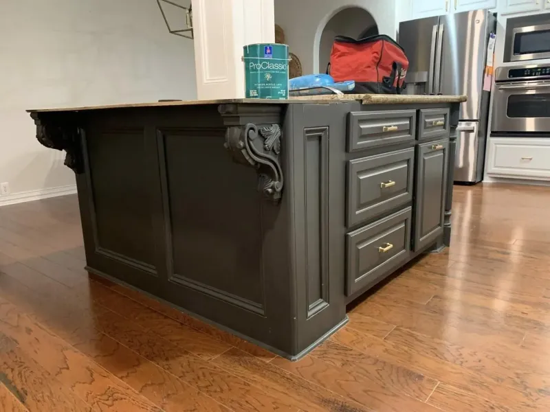 Dark gray kitchen island with decorative accents, drawers, and countertop, on a hardwood floor.
