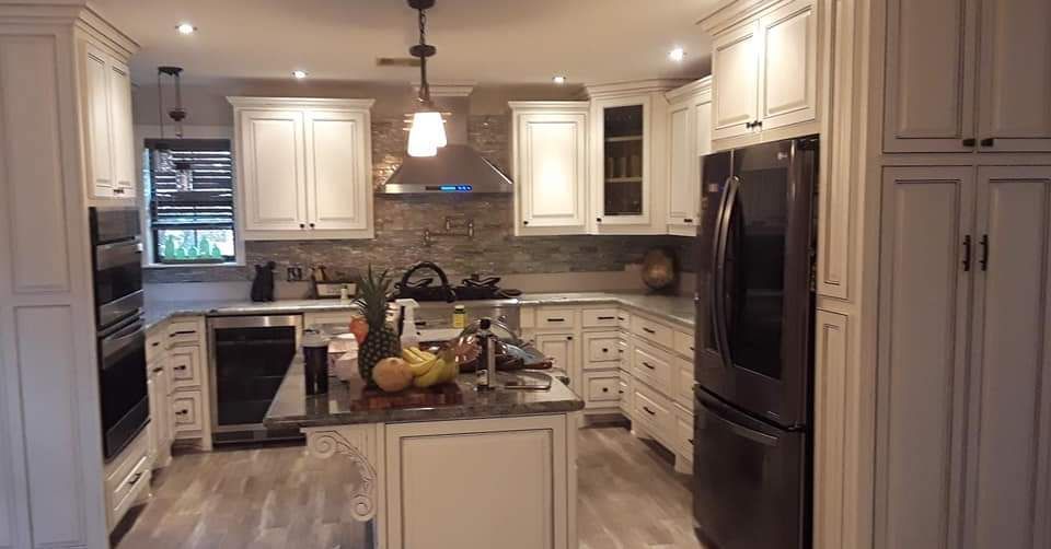 A kitchen with white cabinets, black appliances, and a stone backsplash; island with fruit.