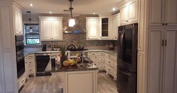 A kitchen with white cabinets, a dark island, stainless steel appliances, and a stone backsplash.