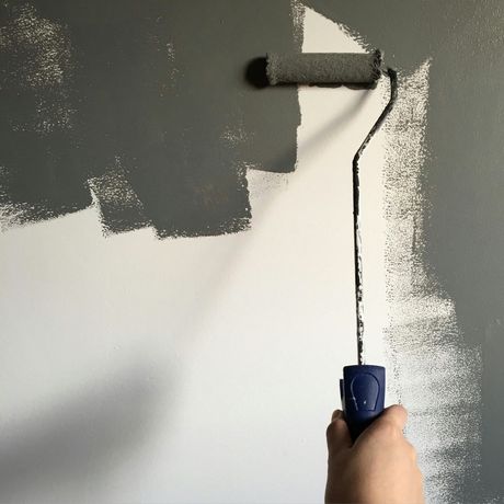 Hand using a paint roller, painting a wall from white to grey.