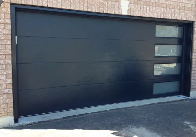 A black garage door with a brick building in the background