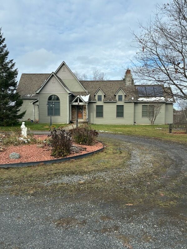 Tan house with brown roof, curved driveway, and landscaping on a cloudy day.