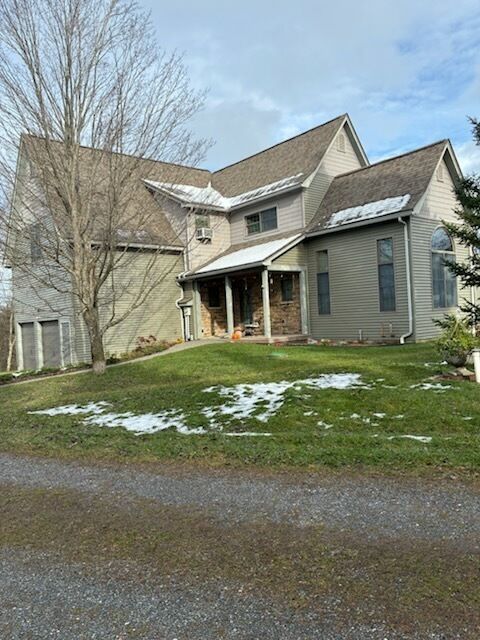 Two-story house with tan siding, brown roof, and small patches of snow on the grass.
