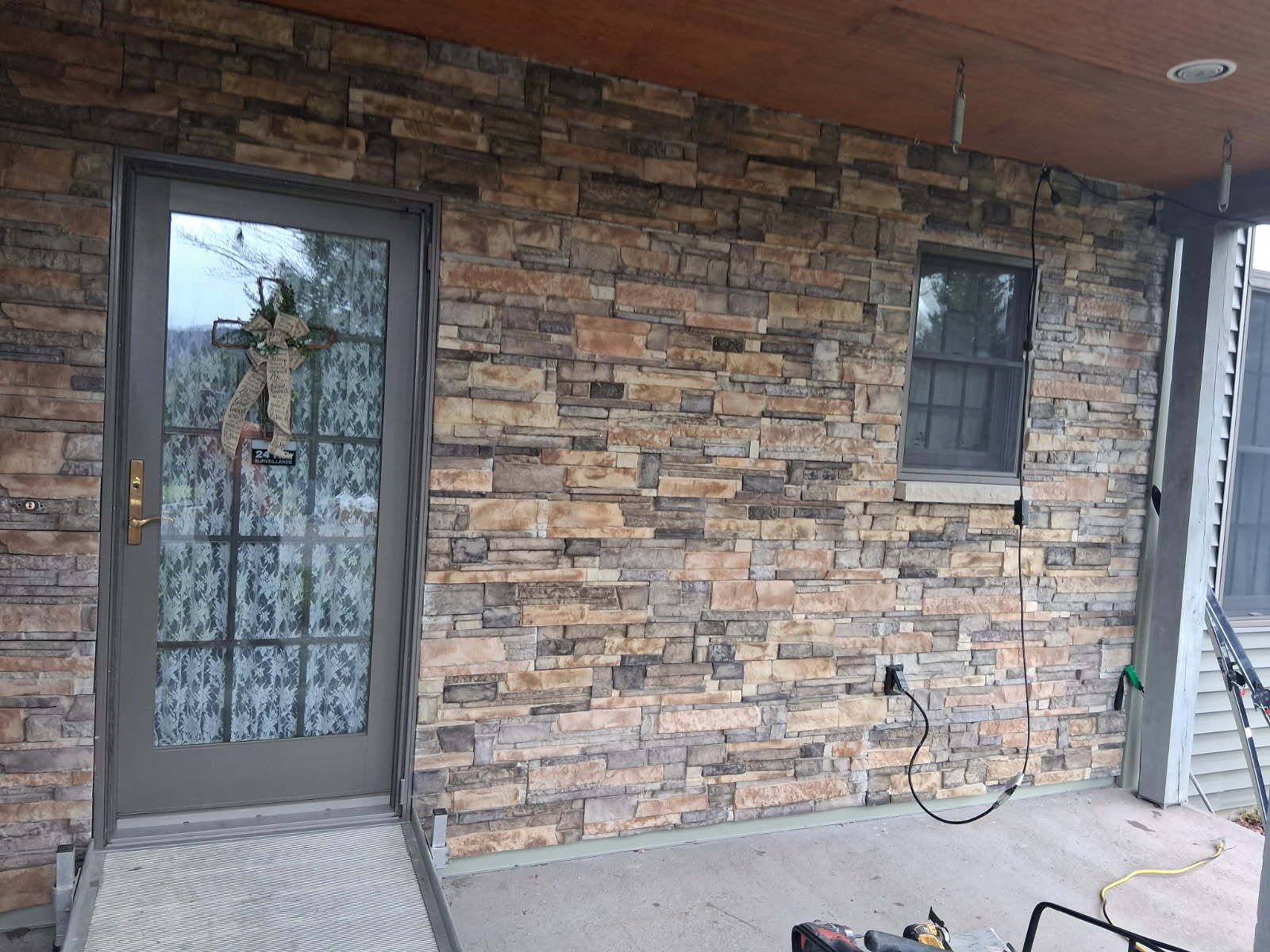 Stone-clad building exterior with a glass door, small window, and porch. Brown, gray, and tan stone.