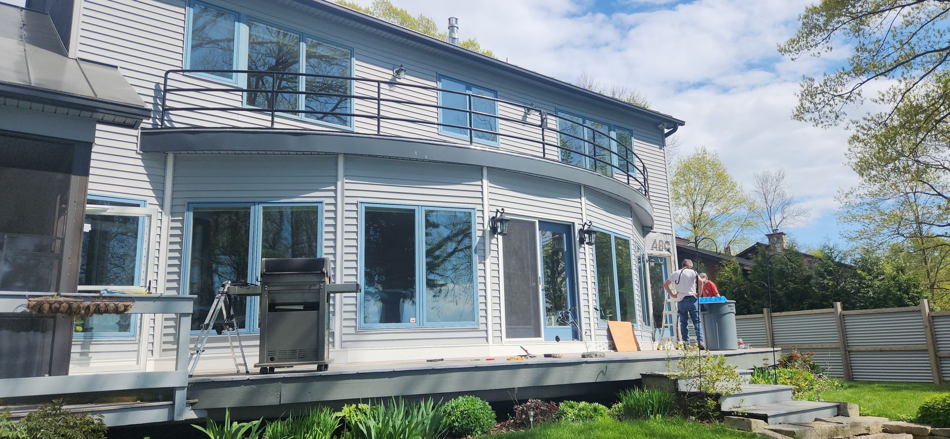 A two-story, curved white house with many windows. A person stands on the deck.