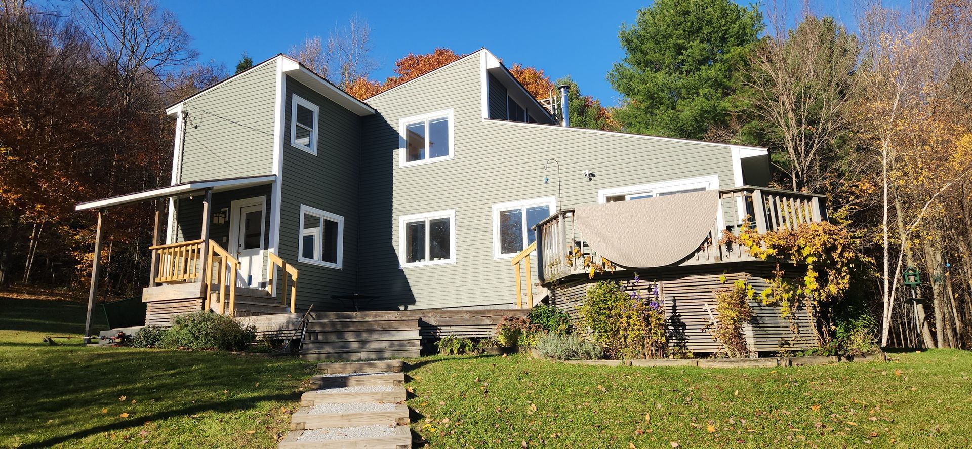 A two-story house with green siding and a sloped roof. A porch and deck extend from the house.