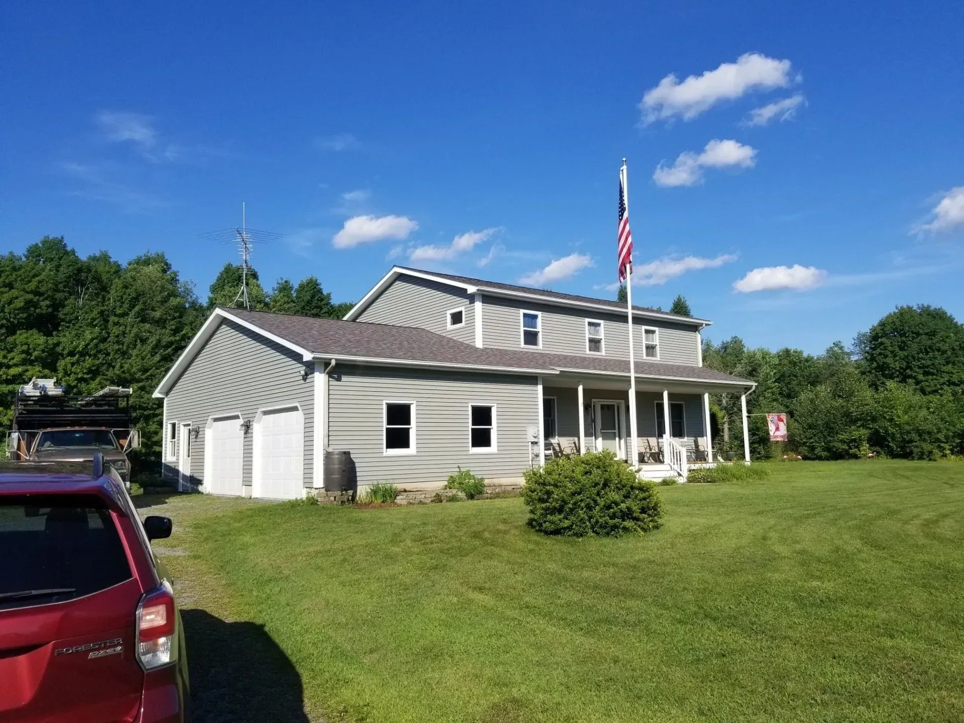 Two-story gray house with garage, porch, and American flag on a sunny day.