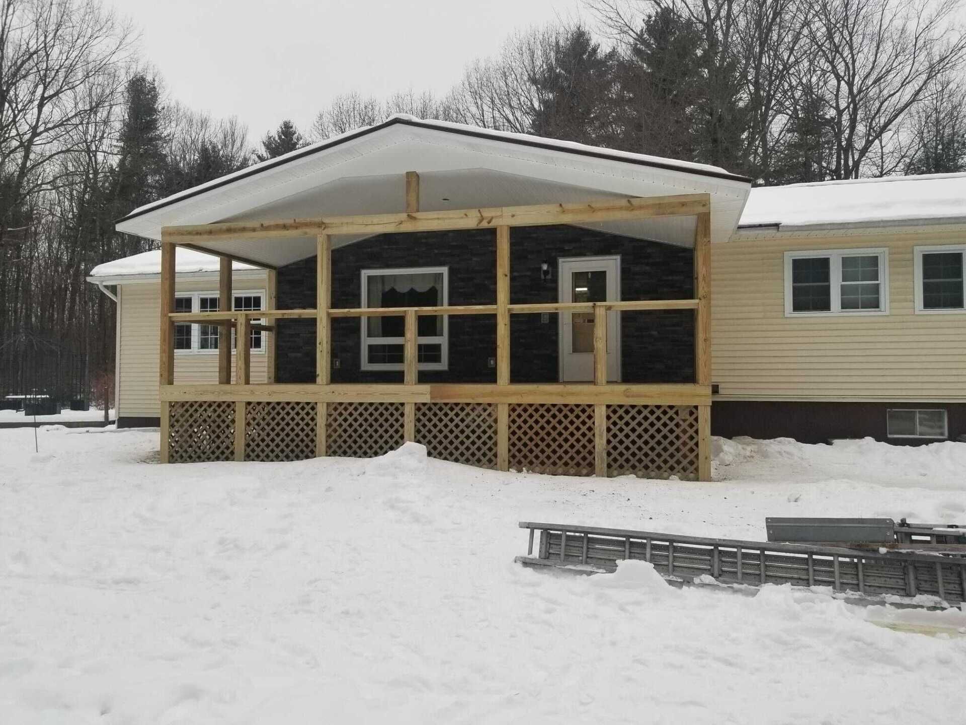 House with wooden porch under construction, covered in snow.