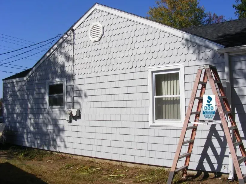 Side view of a house with white shingle siding, a ladder, and a window.