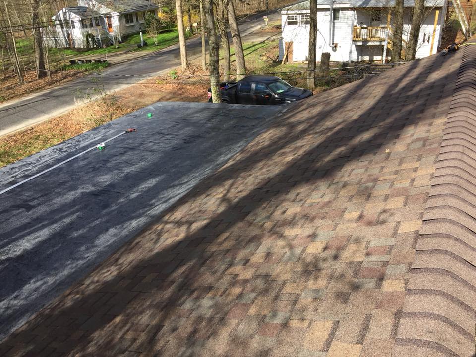 View of a shingled roof with a dark tarp section; a parked black vehicle sits on adjacent land.