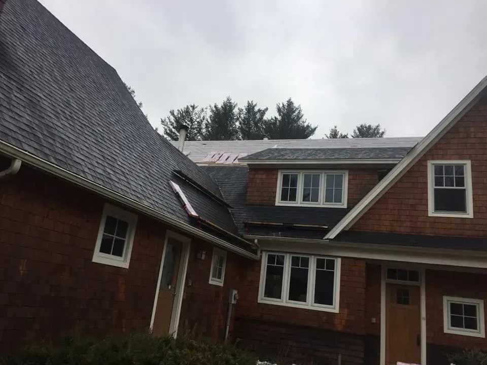 House with brown cedar shake siding, dark roof, and windows, overcast sky.