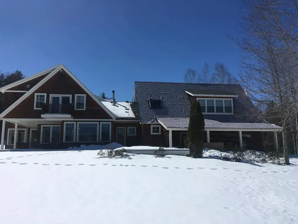 Red house with snow-covered lawn, bright blue sky.