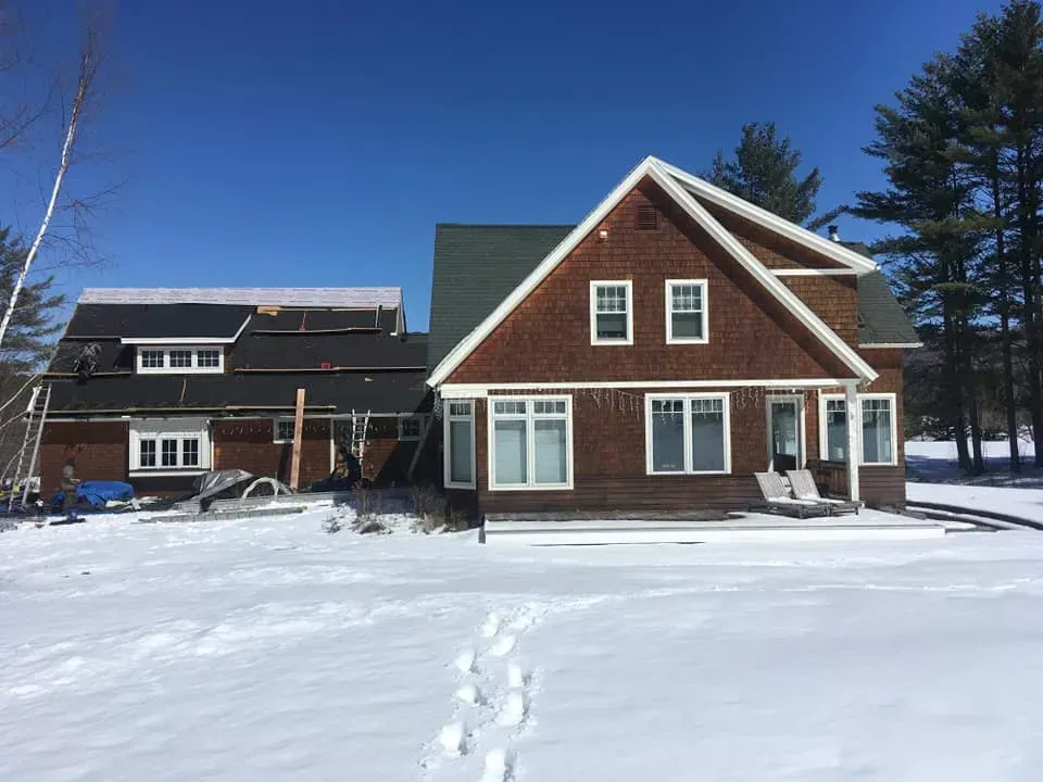 Two-story brown house with white trim and snow-covered ground under a clear blue sky.