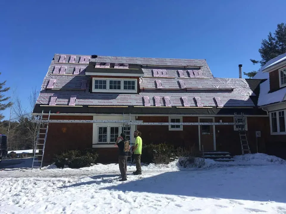Workers on a snowy day installing insulation on a house roof. Blue sky.