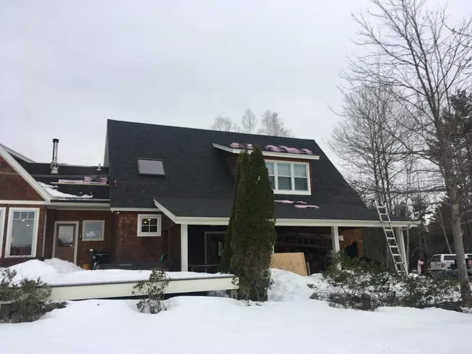 House under construction in winter with snow. New dark roof, scaffolding, and porch.
