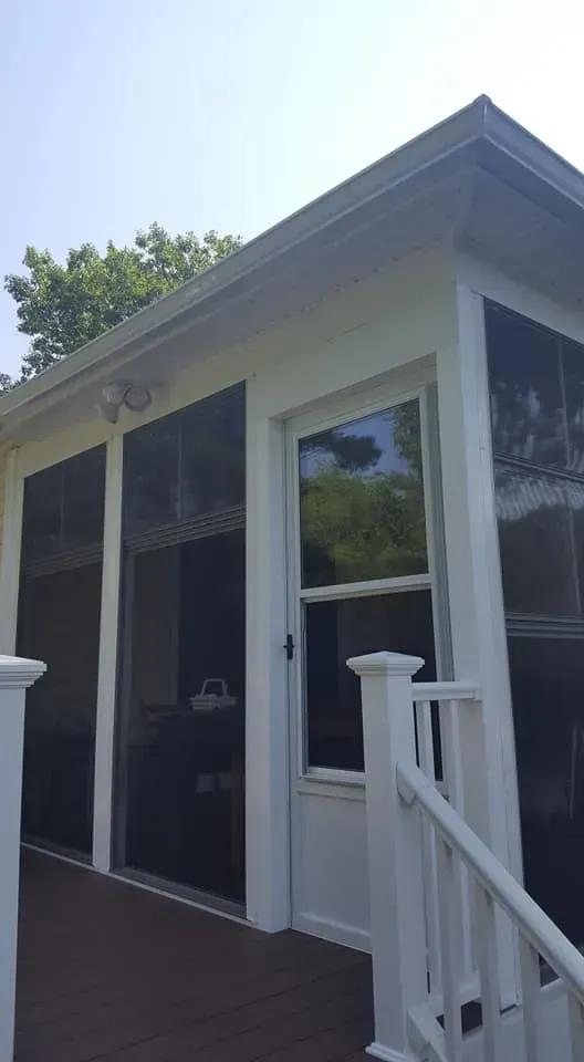 White screened-in porch with door and window; railing on a wooden deck.