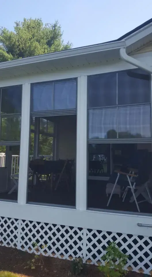 Screened-in porch with white trim and lattice skirting; windows with dark screens and a view of indoor furniture.