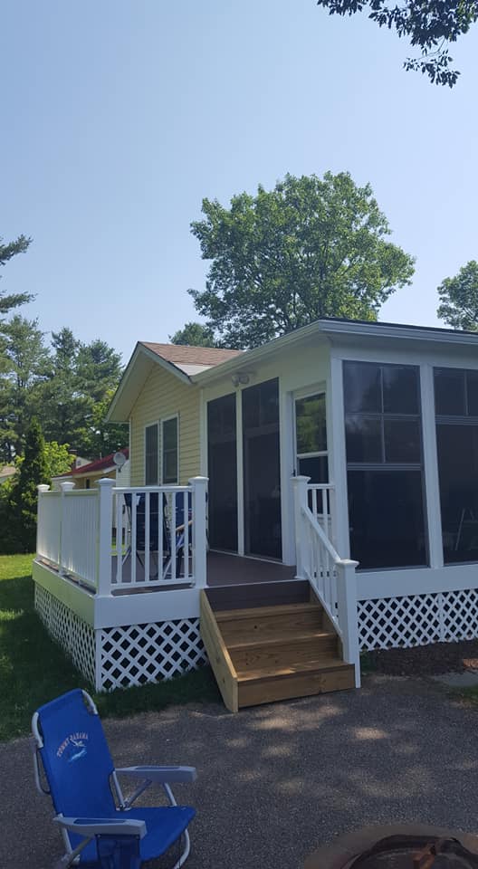 Yellow house with white deck, screened porch, and blue lawn chair on sunny day.