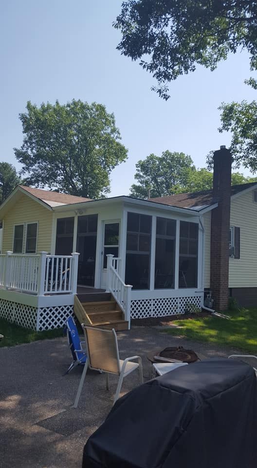 Yellow lake house with white deck and screened porch; sunny day.
