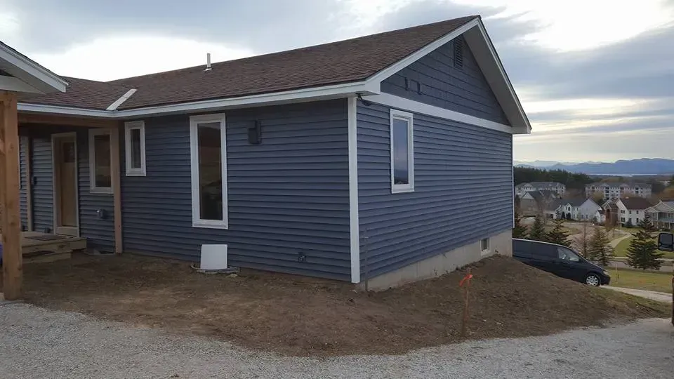 Blue sided house with white trim, brown roof, and small yard.