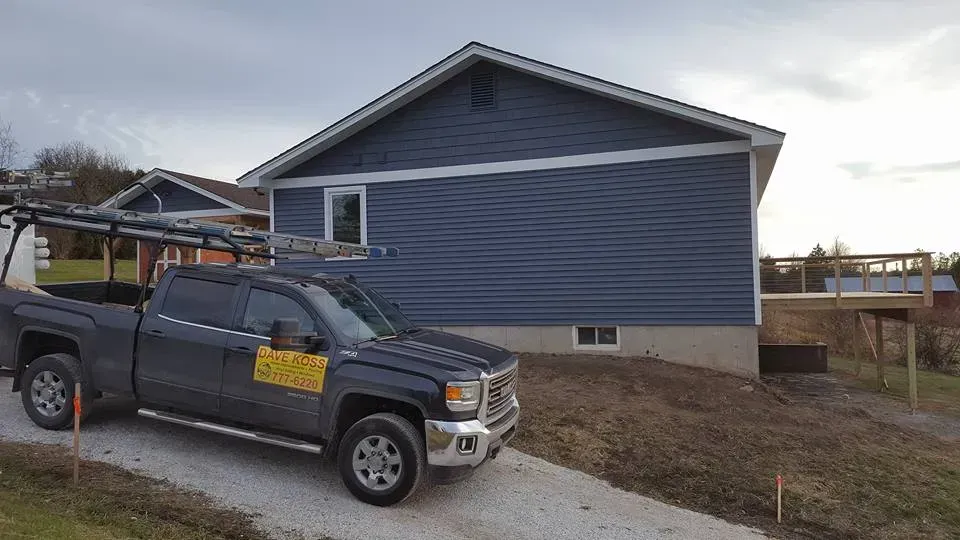 Dark pickup truck parked in front of a blue-sided house with a new deck; construction site.