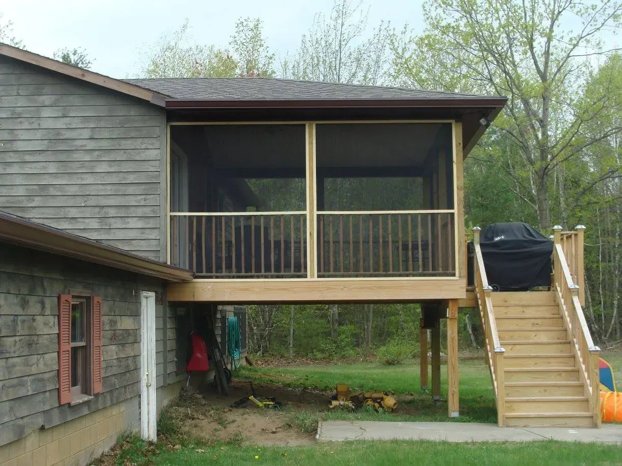 Screened porch with stairs attached to a house with wooden siding.