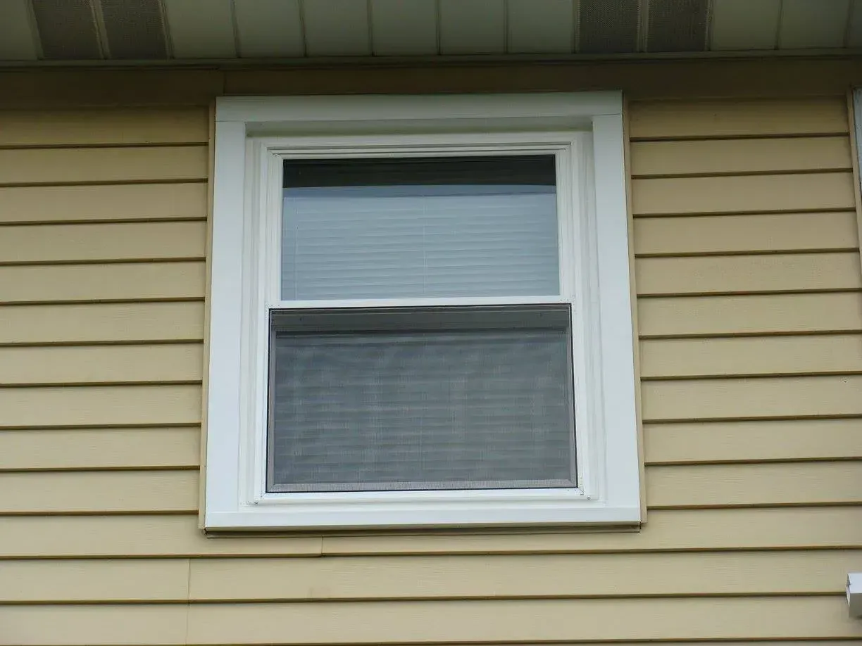 White-framed window on a yellow-sided house with a screen.