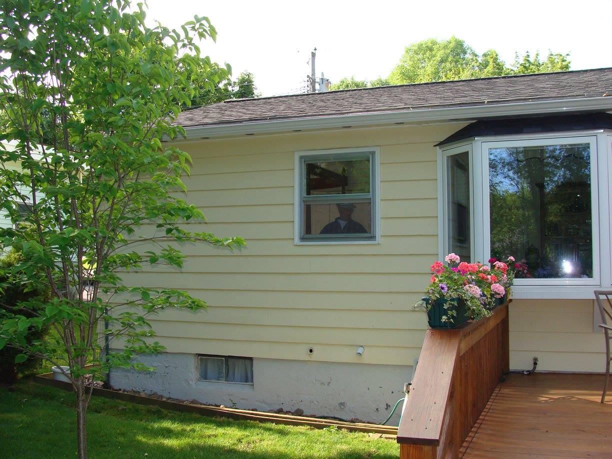 Yellow house exterior with window, bay window, and wooden deck with flower boxes.