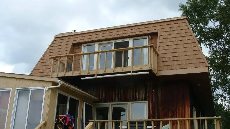 Brown-roofed house with balcony. Wooden exterior, glass windows, cloudy sky.