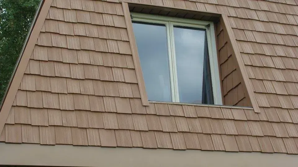 Brown shingled A-frame house with window, light-colored trim.