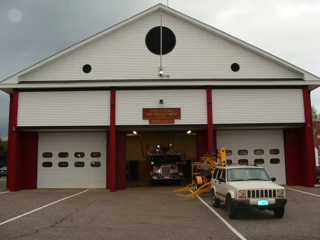 Fire station with white doors, red trim, and a truck inside. A Jeep is parked in front.