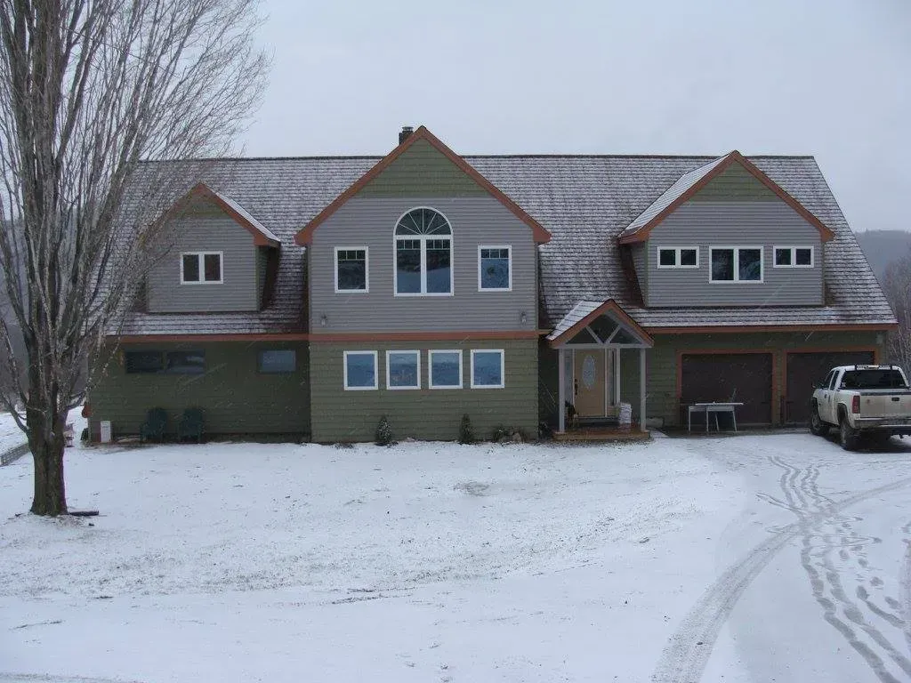 Two-story green and gray house covered in snow with a truck parked in the driveway.