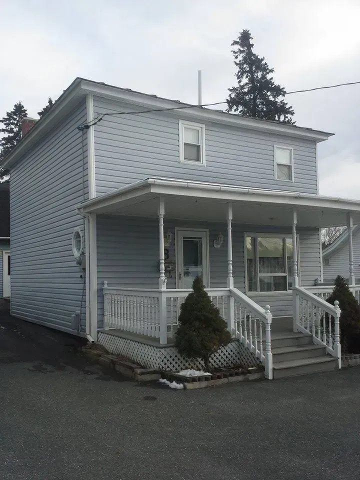 Two-story house with light blue siding, white porch with railing, and steps leading to the front door.