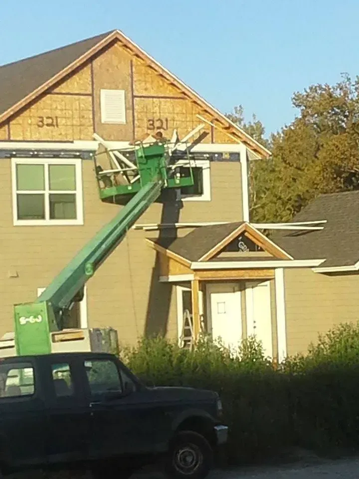A green lift platform next to a house under construction; a truck is in front.
