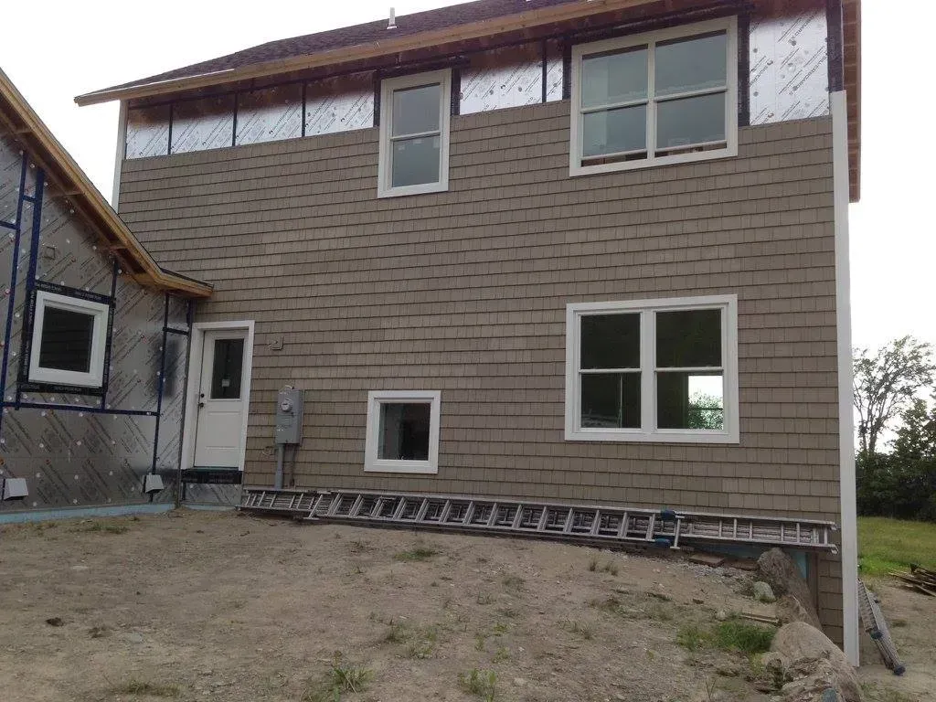 Construction site with a partially sided two-story house, windows, and a ladder.