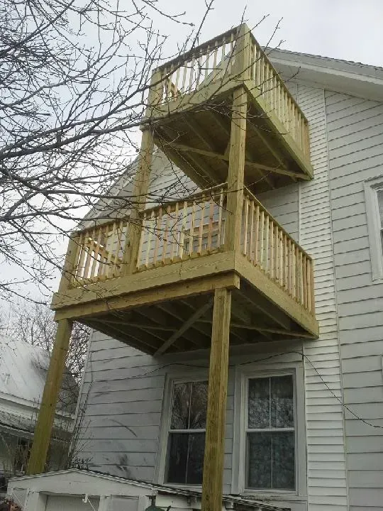 Two-story wooden deck attached to a white house with railings and supporting posts.