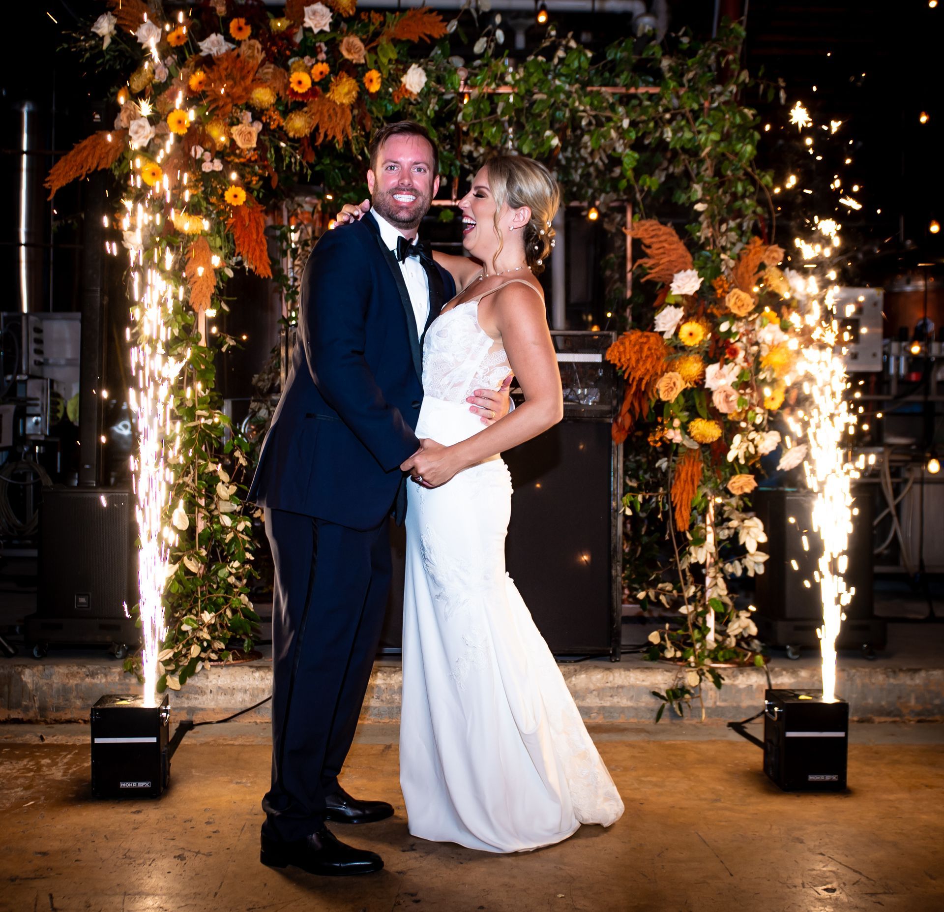 A bride and groom are posing for a picture in front of sparklers.