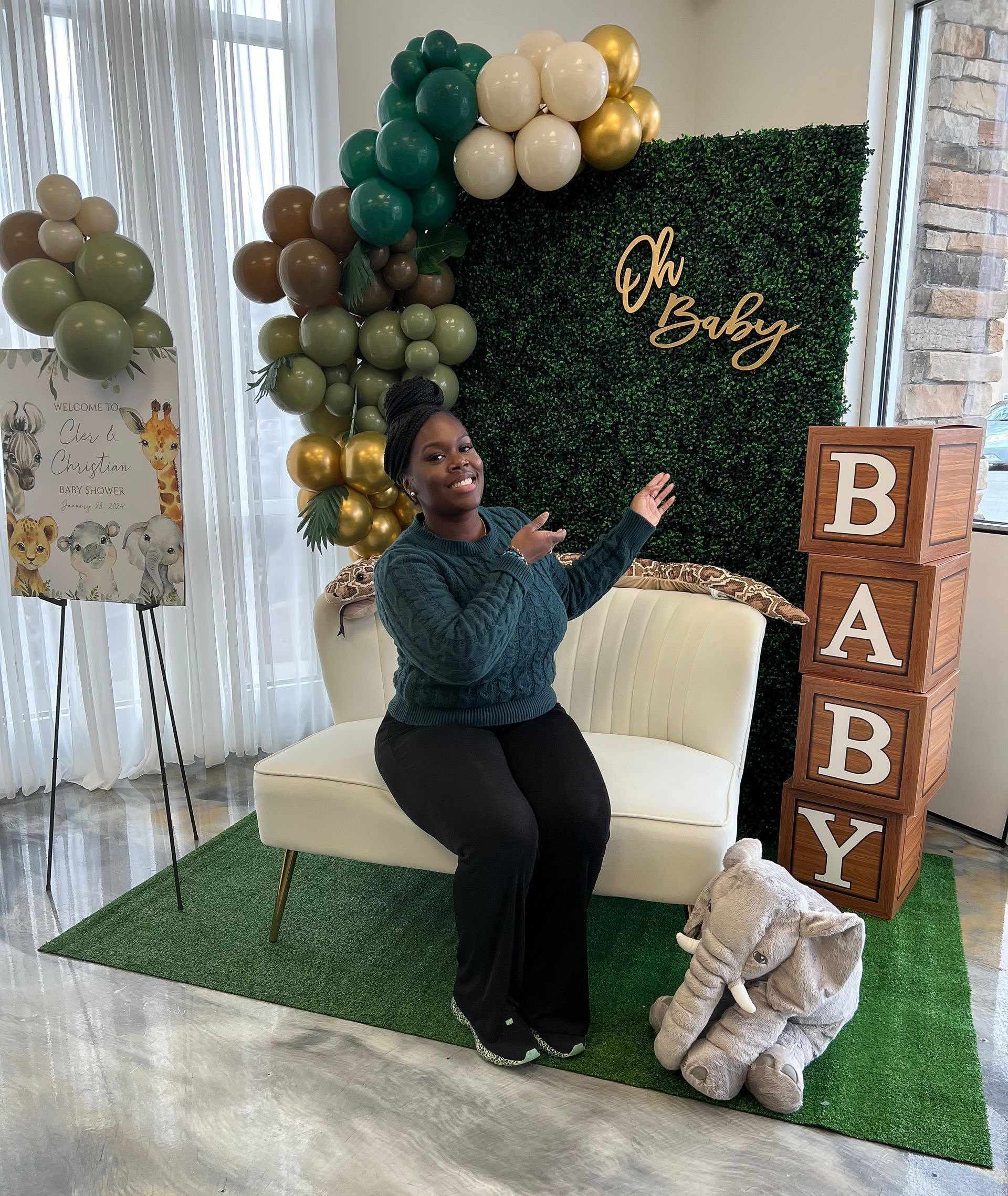 A woman is sitting on a chair in front of a baby shower backdrop.