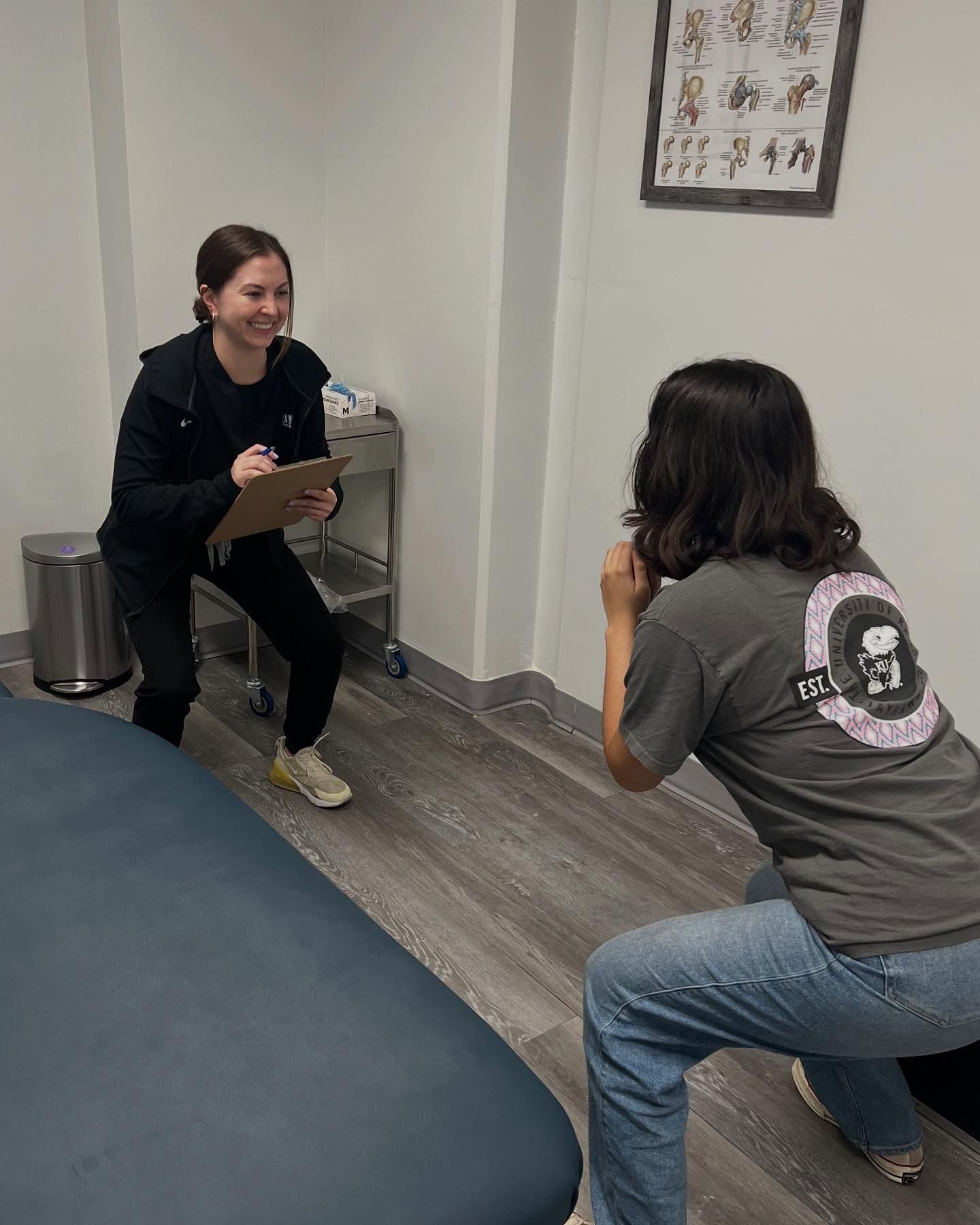 Woman observing another perform a squat in an exam room.