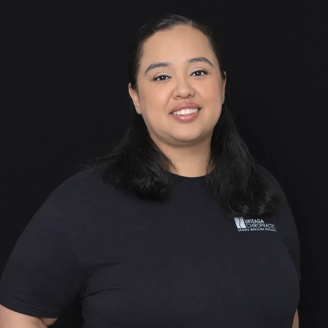Woman with dark hair wearing a black shirt smiles against a black background.
