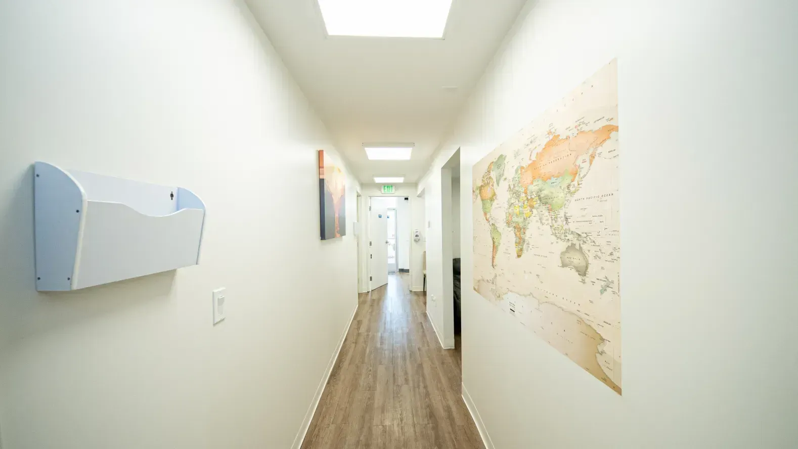 Narrow hallway with white walls, wood-look floor, map, and a wall-mounted organizer.