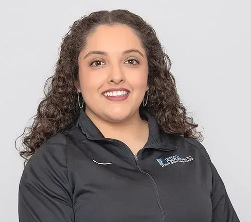 Woman with curly hair smiling in a black jacket; logo on the right.