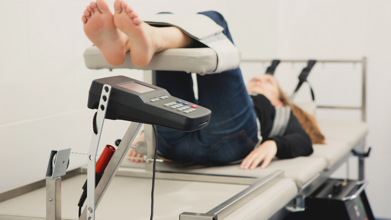 Woman undergoing spinal decompression therapy on a medical table, feet raised.