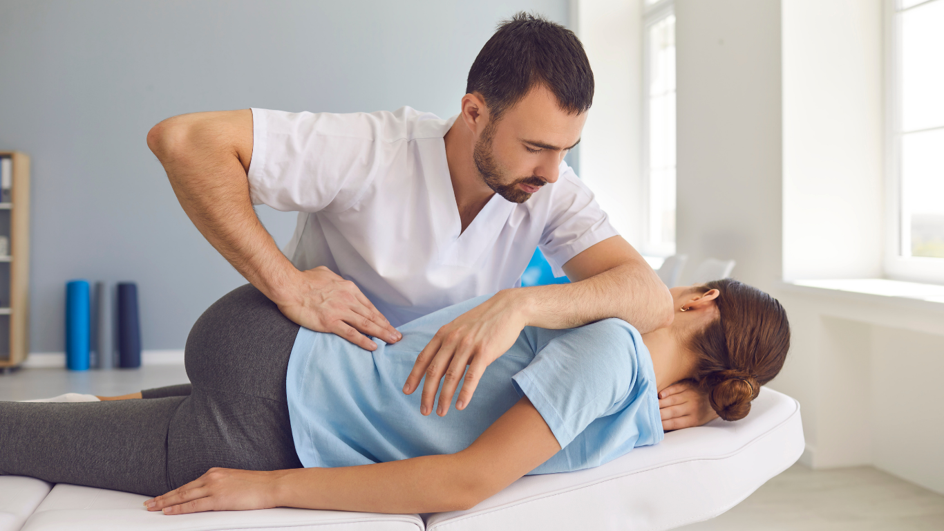 Chiropractor adjusting a patient's back on a therapy table in a light-filled room.