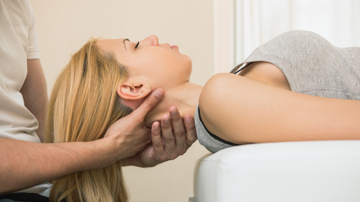 Woman receiving neck adjustment from therapist, lying on a table.