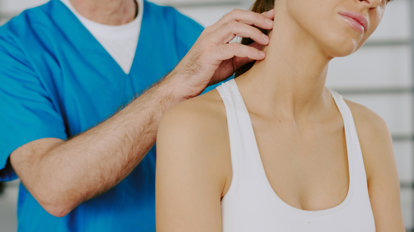 Chiropractor examining a woman's neck; blue scrubs, white top, neutral setting.