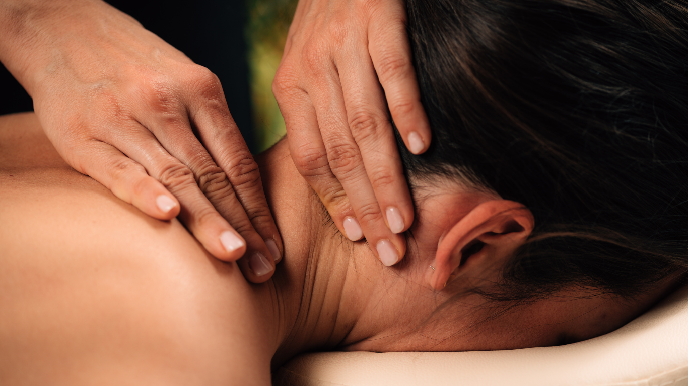 Hands massaging a person's neck and shoulders, close-up, outdoors.